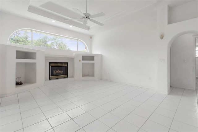 16 Birchwood Pl, Palm Coast, FL 32137 - unfurnished living room featuring a glass covered fireplace, arched walkways, recessed lighting, a raised ceiling, and light tile patterned floors