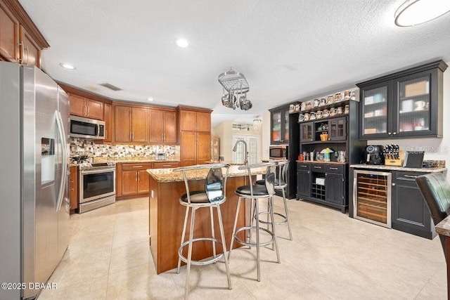 3959 S Chinook Ln, Ormond Beach, FL 32174 - kitchen with stainless steel appliances, beverage cooler, light stone counters, a kitchen bar, and brown cabinets