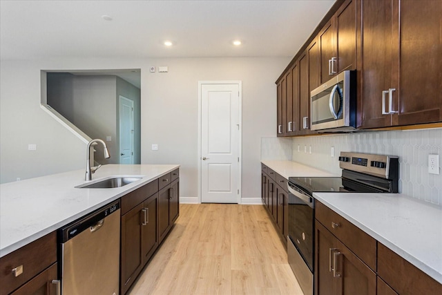 kitchen featuring tasteful backsplash, appliances with stainless steel finishes, dark brown cabinets, light wood-style floors, and a sink