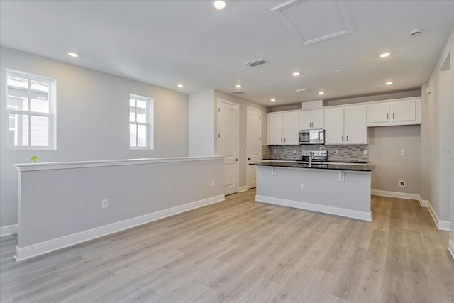 kitchen featuring stainless steel appliances, an island with sink, dark countertops, and white cabinetry