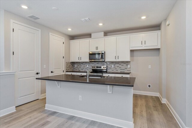 kitchen featuring dark countertops, white cabinetry, a center island with sink, and appliances with stainless steel finishes