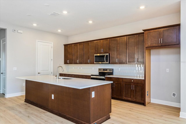 kitchen with light countertops, appliances with stainless steel finishes, a sink, and a center island with sink