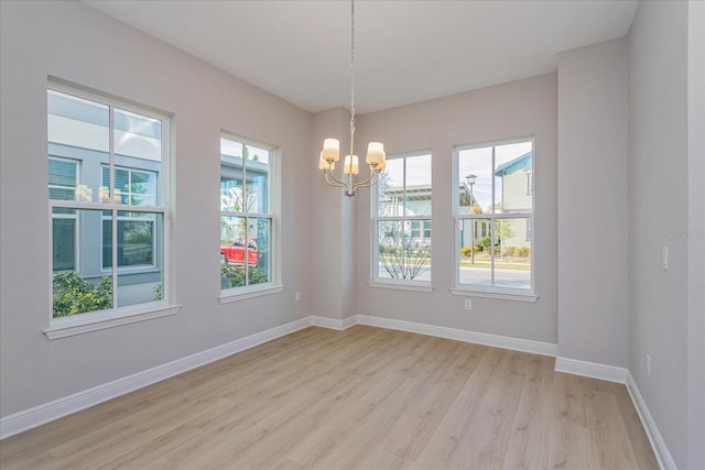 spare room with light wood-style floors, an inviting chandelier, a wealth of natural light, and baseboards