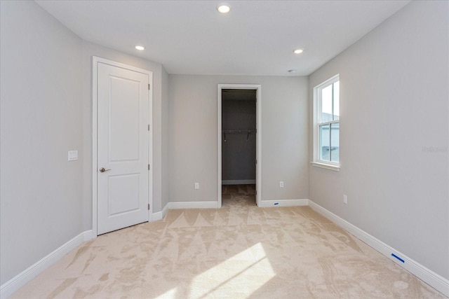 unfurnished bedroom with light carpet, a spacious closet, and baseboards