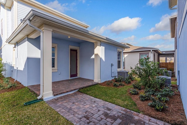 rear view of property featuring a yard, central AC, and stucco siding