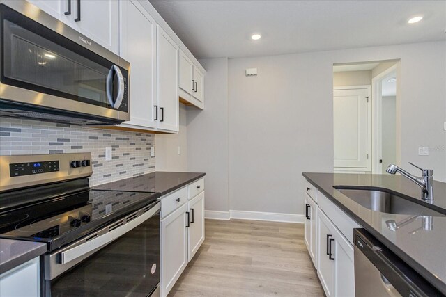 kitchen featuring appliances with stainless steel finishes, a sink, white cabinetry, and light wood-style floors