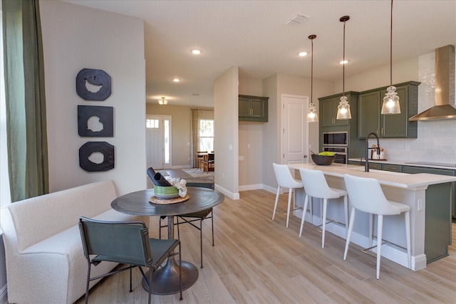 kitchen featuring backsplash, light hardwood / wood-style flooring, wall chimney range hood, a breakfast bar area, and pendant lighting