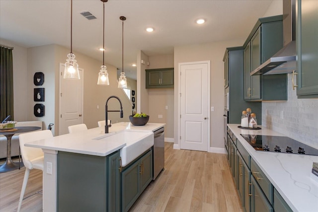 kitchen featuring light hardwood / wood-style floors, decorative light fixtures, wall chimney exhaust hood, black electric stovetop, and a kitchen island with sink