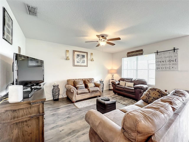 living room with a textured ceiling, ceiling fan, and wood-type flooring