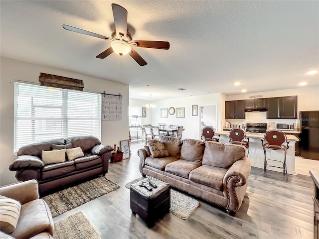 living room with a textured ceiling, light hardwood / wood-style floors, and ceiling fan with notable chandelier