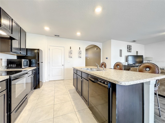 kitchen featuring an island with sink, light tile flooring, a breakfast bar, appliances with stainless steel finishes, and sink