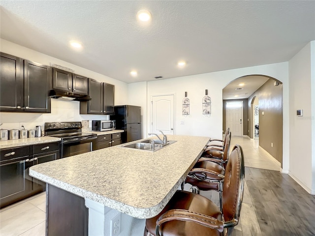 kitchen featuring light tile floors, appliances with stainless steel finishes, a breakfast bar area, and an island with sink