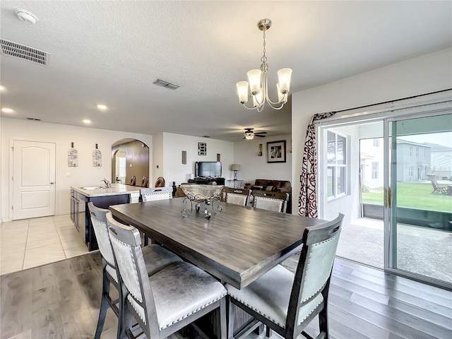 dining room with a textured ceiling, ceiling fan with notable chandelier, sink, and light hardwood / wood-style flooring