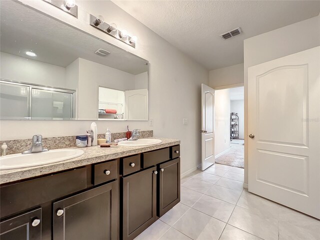 bathroom with double vanity, tile flooring, and a textured ceiling