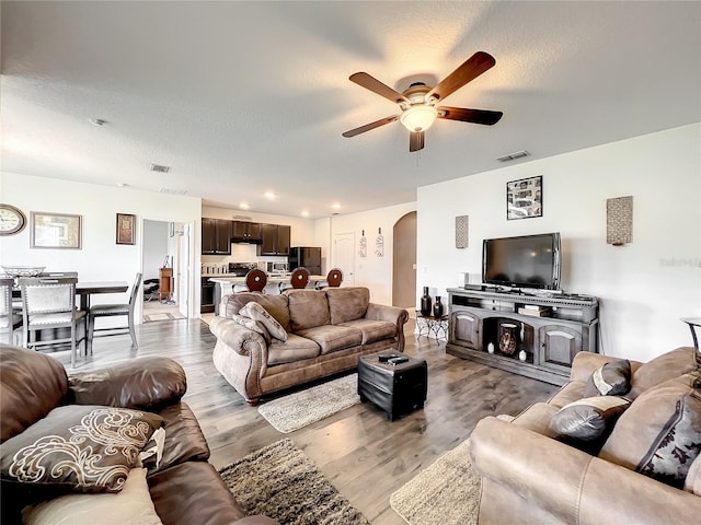 living room with ceiling fan, light hardwood / wood-style flooring, and a textured ceiling