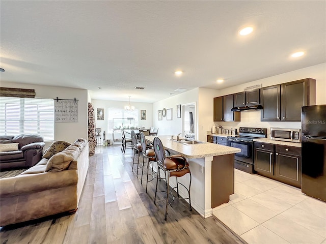 kitchen with hanging light fixtures, black appliances, a kitchen island with sink, a chandelier, and a breakfast bar area