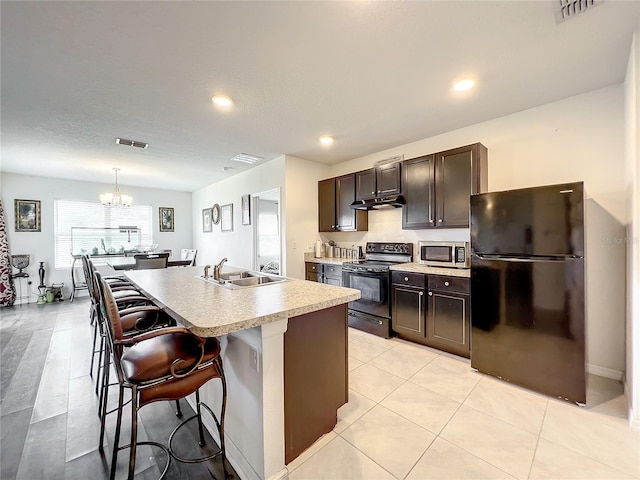 kitchen featuring a kitchen breakfast bar, a notable chandelier, a center island with sink, black appliances, and sink