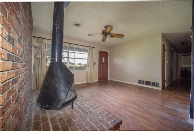 interior space with ceiling fan, dark wood-type flooring, a wood stove, brick wall, and a textured ceiling