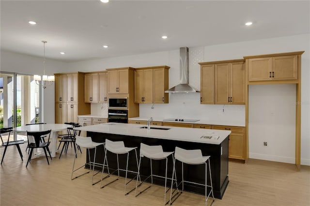 kitchen featuring black appliances, an island with sink, hanging light fixtures, and wall chimney exhaust hood