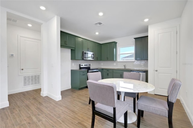 kitchen with stainless steel appliances, sink, backsplash, and green cabinetry