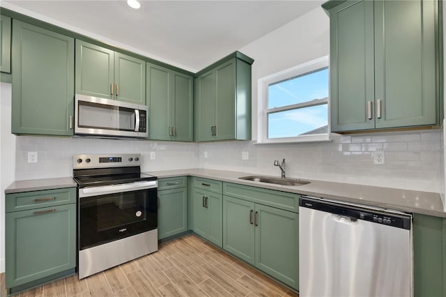 kitchen with sink, light hardwood / wood-style flooring, stainless steel appliances, green cabinetry, and decorative backsplash