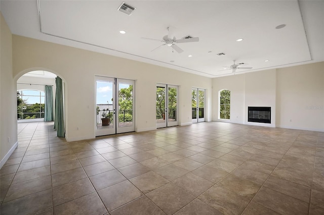 unfurnished living room with a tray ceiling, ceiling fan, and light tile flooring