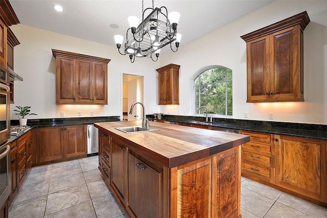 kitchen featuring an island with sink, sink, light tile floors, a chandelier, and wood counters