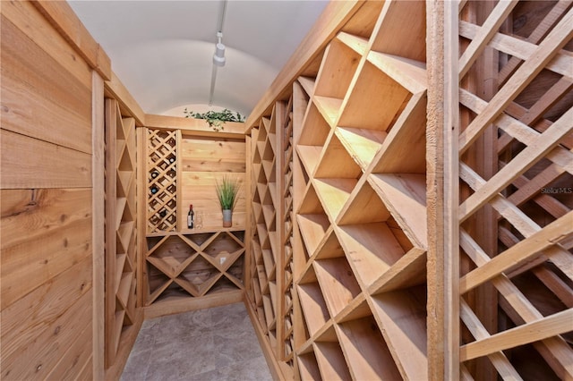 wine room featuring light tile floors, wooden walls, and vaulted ceiling