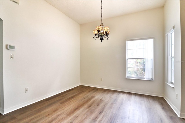 unfurnished room featuring hardwood / wood-style flooring, a notable chandelier, and vaulted ceiling