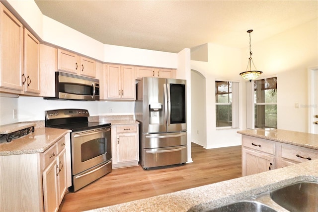 kitchen with decorative light fixtures, light brown cabinetry, appliances with stainless steel finishes, and light hardwood / wood-style flooring