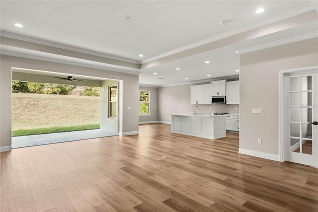 unfurnished living room featuring crown molding, light hardwood / wood-style floors, ceiling fan, and sink