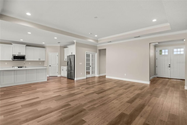 unfurnished living room with french doors, ornamental molding, a raised ceiling, and light wood-type flooring