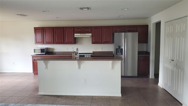 kitchen featuring a center island with sink, a kitchen bar, appliances with stainless steel finishes, and tile flooring