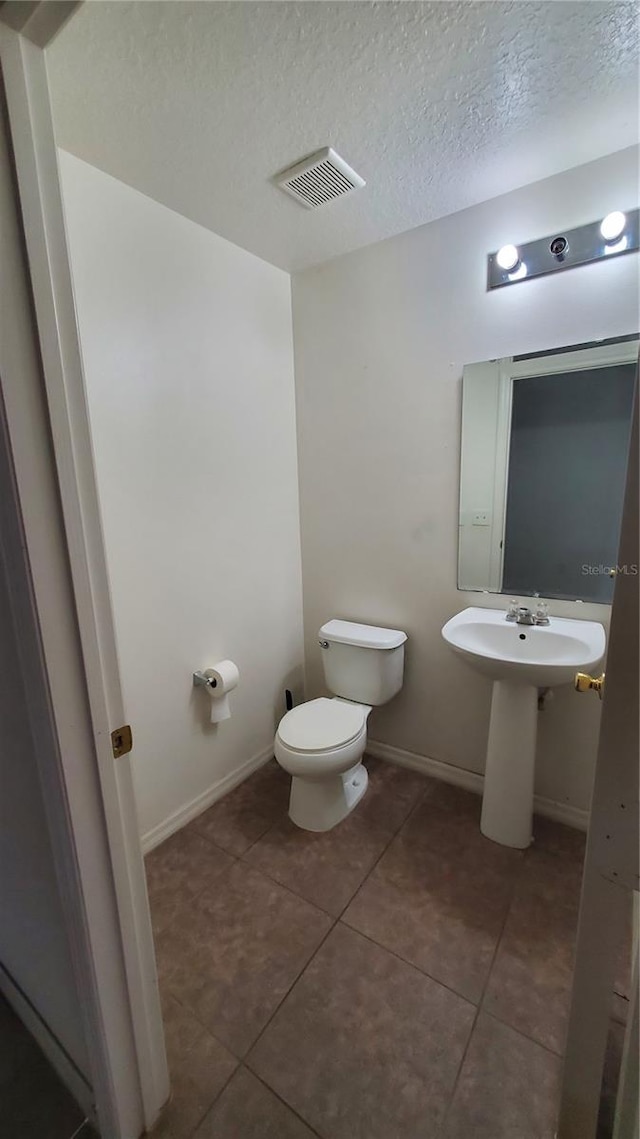 bathroom with tile flooring, a textured ceiling, and toilet