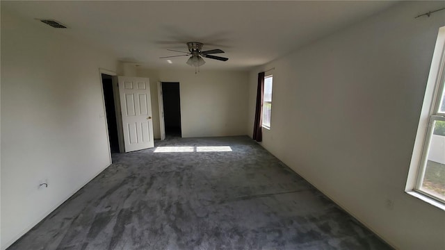 empty room with ceiling fan and dark colored carpet