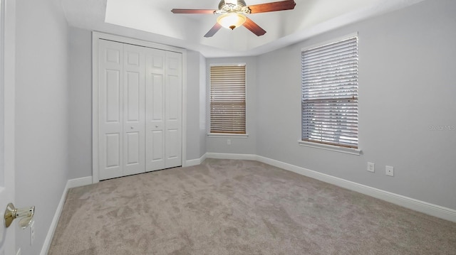 unfurnished bedroom featuring light carpet, a tray ceiling, a closet, and ceiling fan