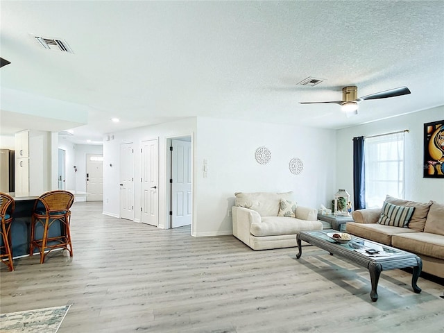 living room featuring a textured ceiling, light wood-type flooring, and ceiling fan