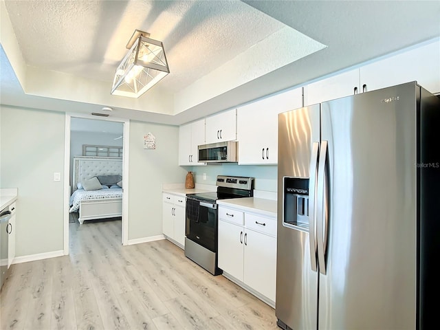 kitchen featuring light wood-type flooring, appliances with stainless steel finishes, a textured ceiling, and white cabinetry