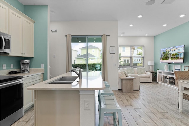 kitchen with a center island with sink, appliances with stainless steel finishes, white cabinetry, light hardwood / wood-style flooring, and sink