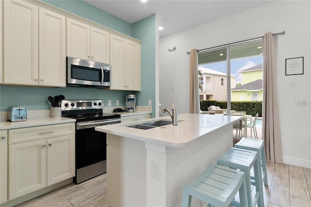 kitchen with appliances with stainless steel finishes, a center island with sink, light stone counters, and sink