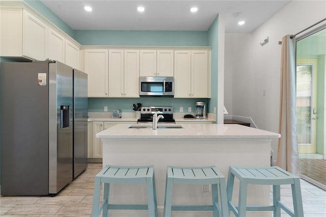 kitchen with appliances with stainless steel finishes, light stone countertops, a kitchen bar, a center island with sink, and white cabinetry