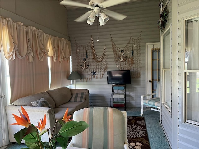 carpeted living room with wooden walls and ceiling fan