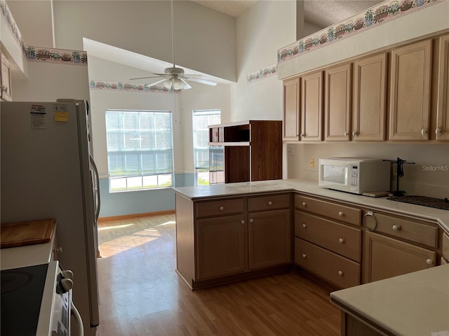 kitchen featuring light wood-type flooring, a textured ceiling, kitchen peninsula, white appliances, and ceiling fan