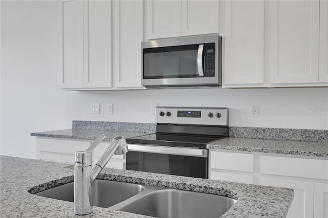 kitchen with white cabinets, stainless steel appliances, sink, and light stone counters