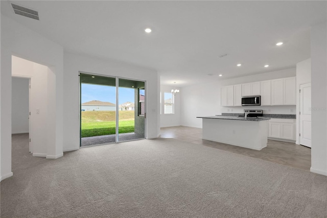 kitchen with white cabinets, appliances with stainless steel finishes, light colored carpet, and an island with sink