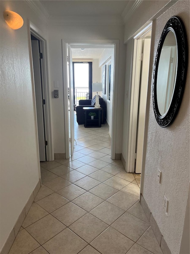 corridor featuring light tile patterned floors, a textured wall, ornamental molding, and baseboards