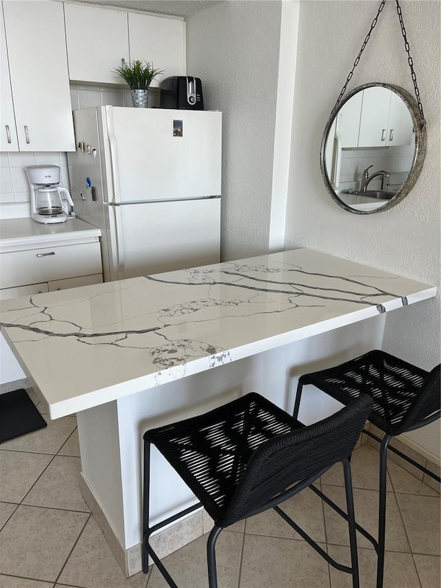 kitchen with freestanding refrigerator, light tile patterned floors, white cabinets, light countertops, and a textured wall