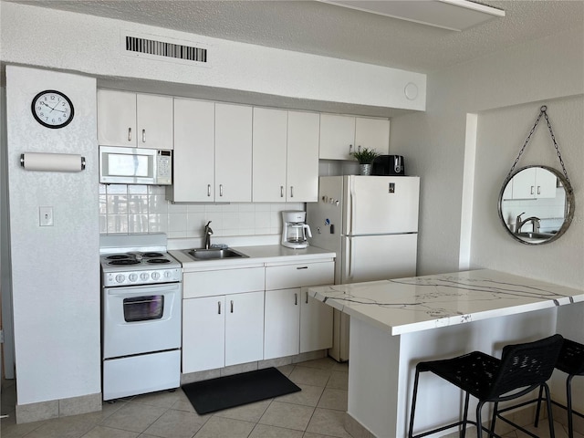 kitchen featuring white cabinets, white appliances, visible vents, and a sink