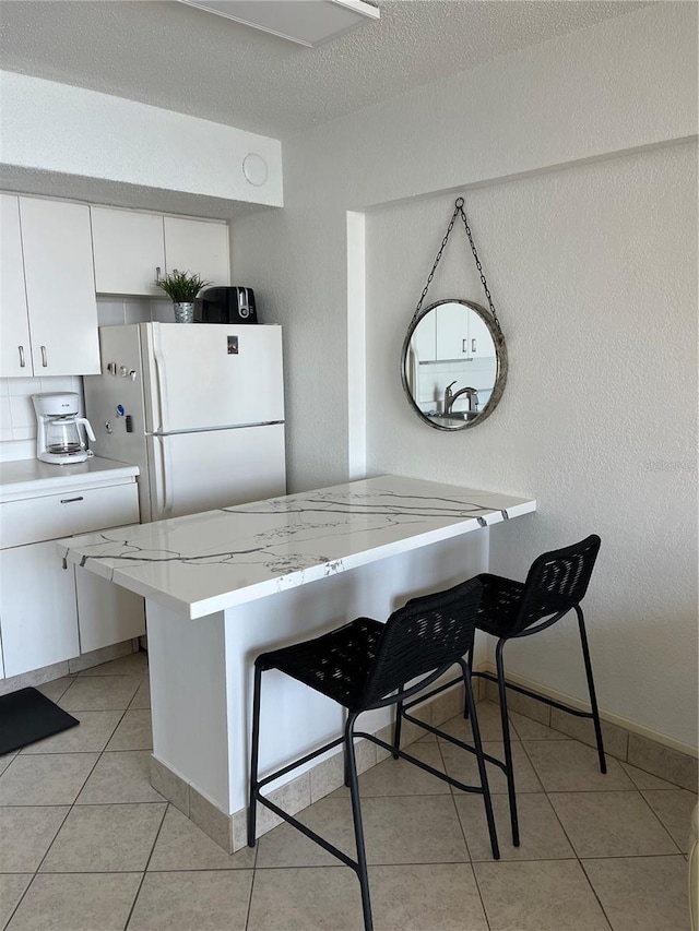 kitchen with a textured wall, freestanding refrigerator, a breakfast bar area, and white cabinetry