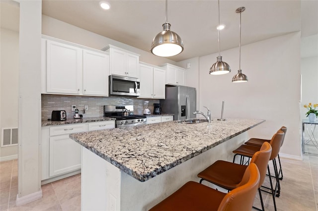 kitchen featuring pendant lighting, light tile floors, tasteful backsplash, appliances with stainless steel finishes, and a breakfast bar area